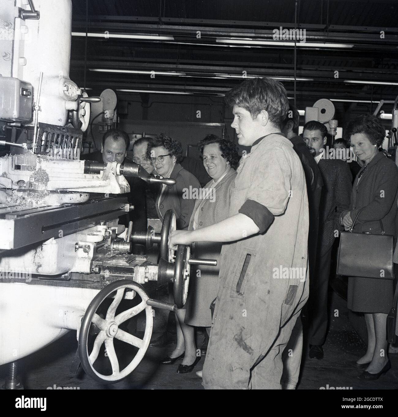 1960s, historical, local councilors and press watching a young male  apprentice using a large mechanical engineering lathe, Kelty, Scotland, UK.  The decline of the traditional coalmining industry and the closing of the