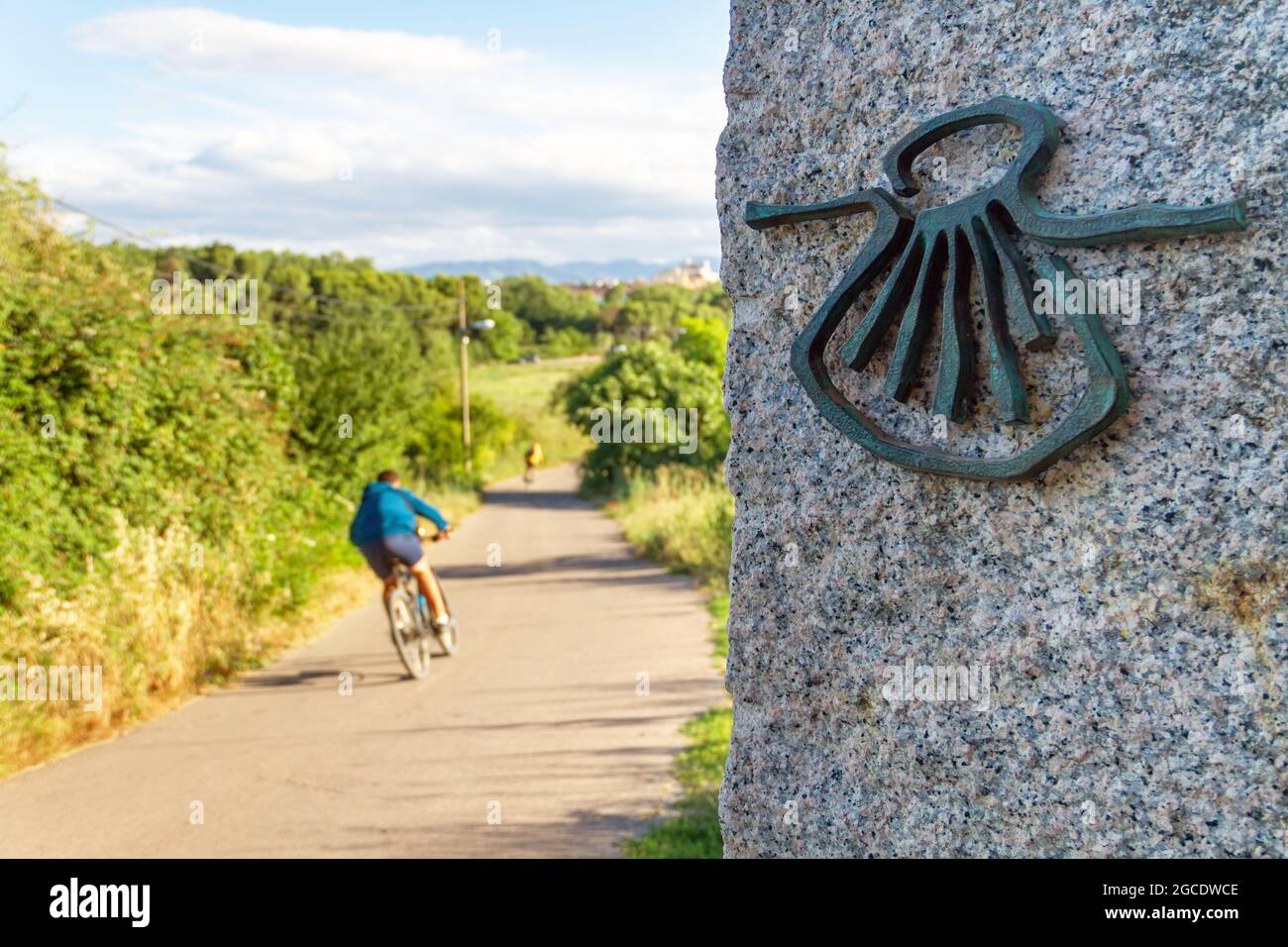 Pilgrim cyclist on the Camino de Santiago (Sant James Way) loaded with a backpack next to a column with the shell symbol of the Camino Santiago de Com Stock Photo