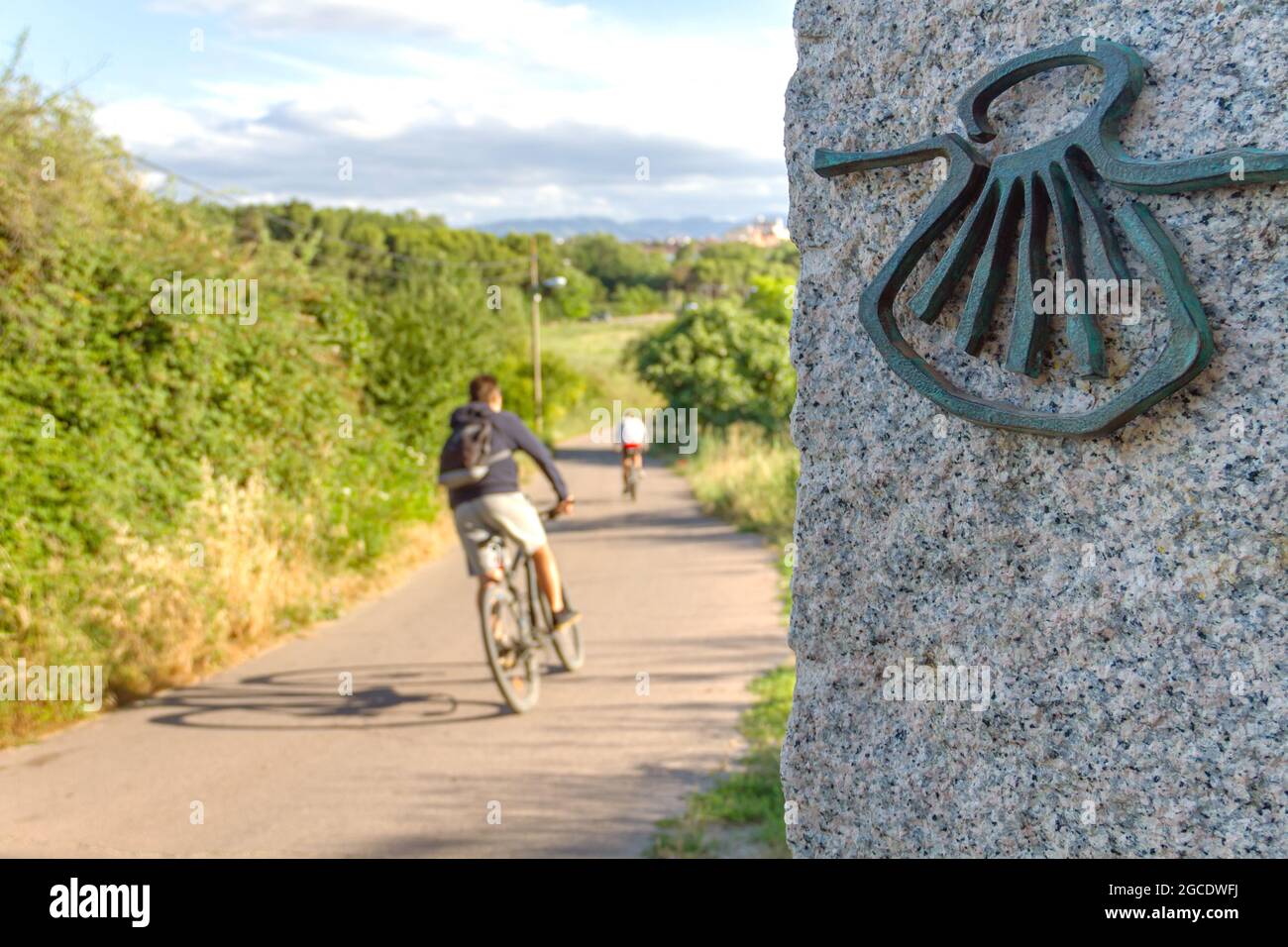 Pilgrim cyclist on the Camino de Santiago (Sant James Way) loaded with a backpack next to a column with the shell symbol of the Camino Santiago de Com Stock Photo