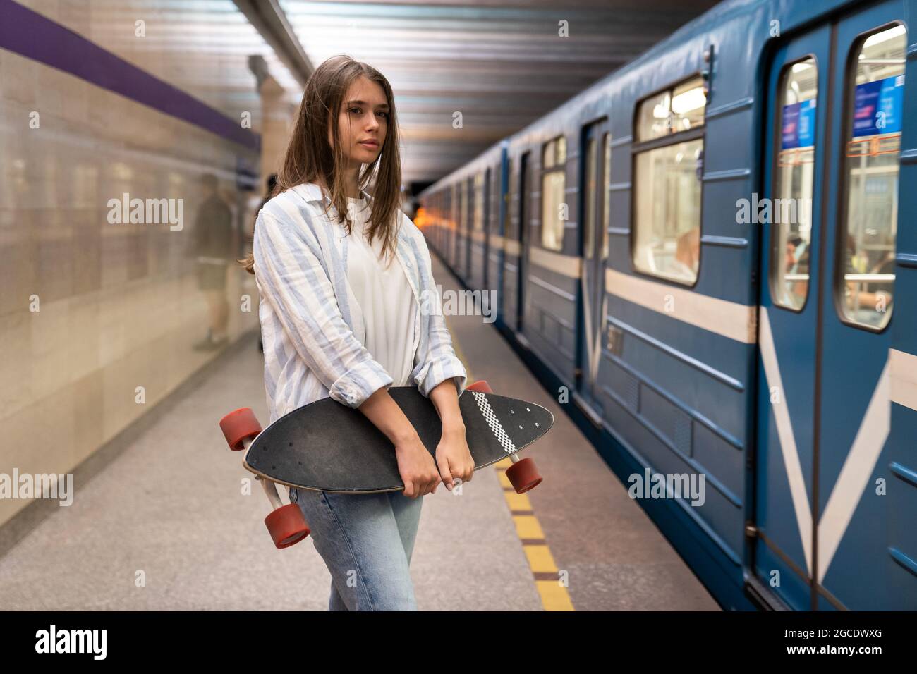 Young girl at metro platform look at subway car at underground metro  station alone holding longboard Stock Photo - Alamy