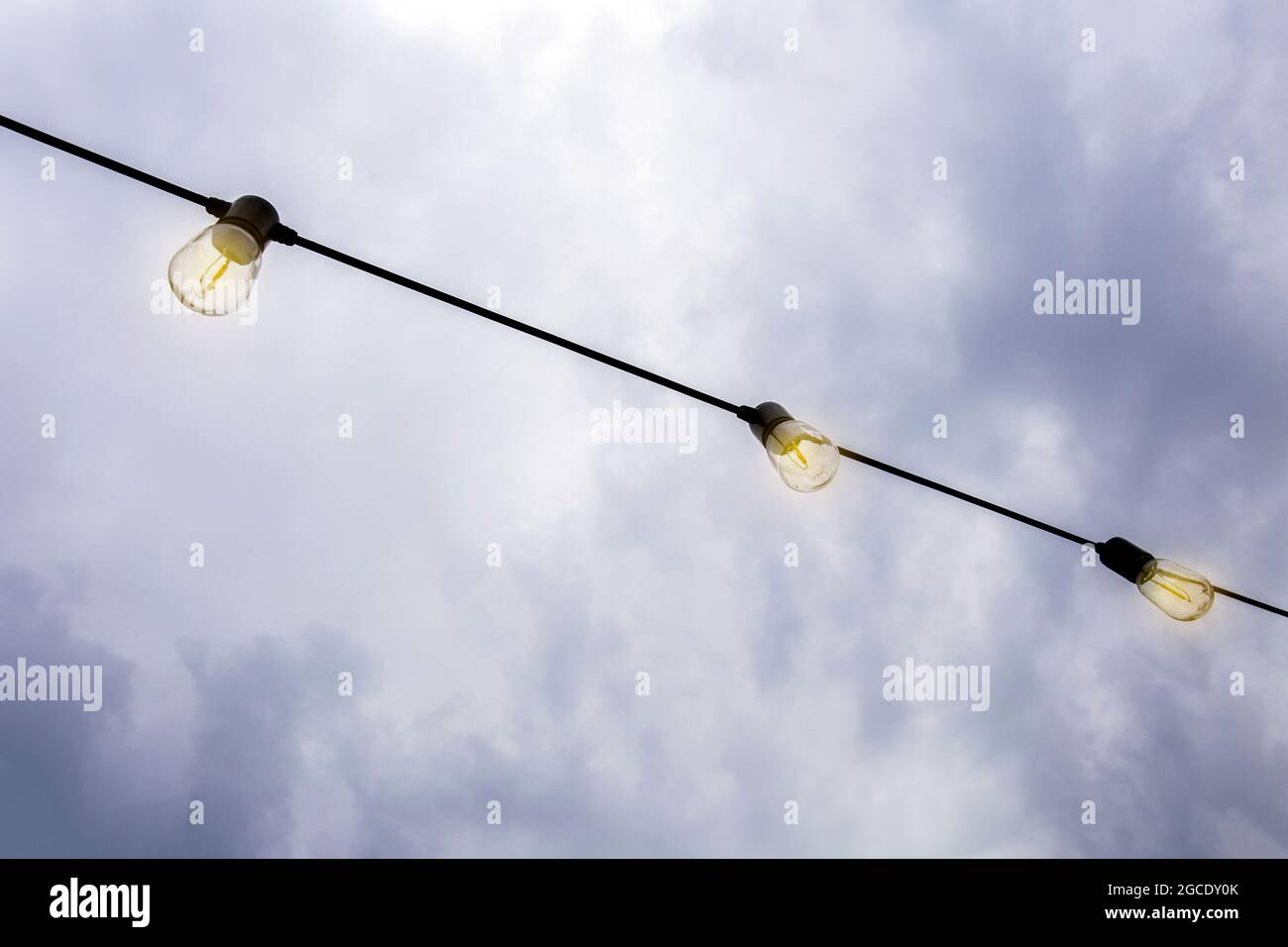 Glowing Light bulbs hanging against the dark evening sky, in a row modern decoration with copy space Stock Photo