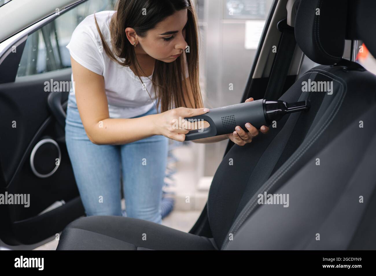 Female using portable vacuum cleaner in her car. Electrical vacuum in