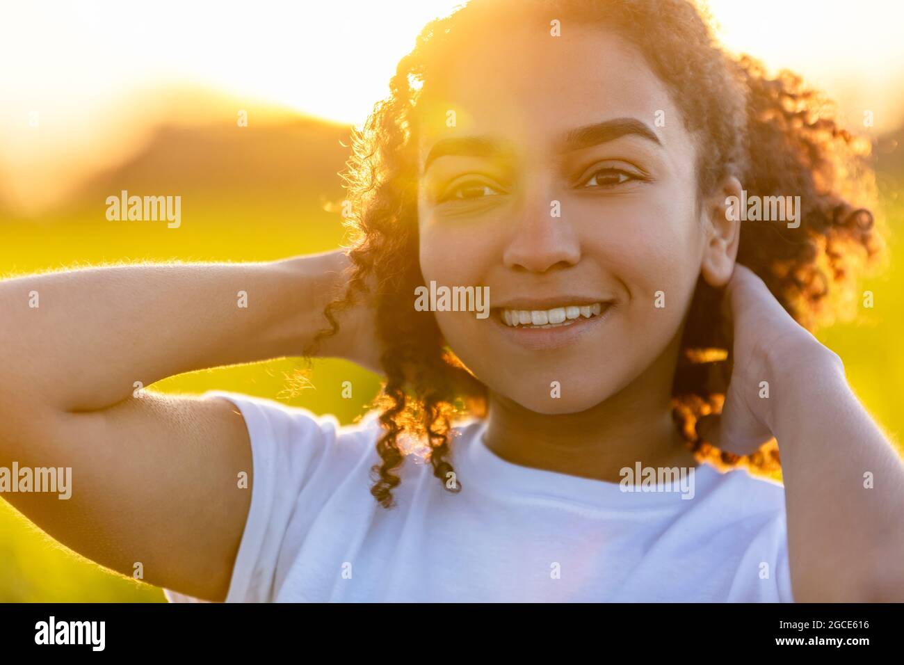 Beautiful biracial mixed race African American teenager teen girl young woman smiling outside backlit at sunset or sunrise Stock Photo