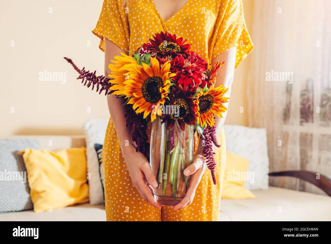 Woman holds vase with sunflowers amaranth and zinnia flowers. Bouquet of fall red yellow orange brown blooms at home. Stock Photo
