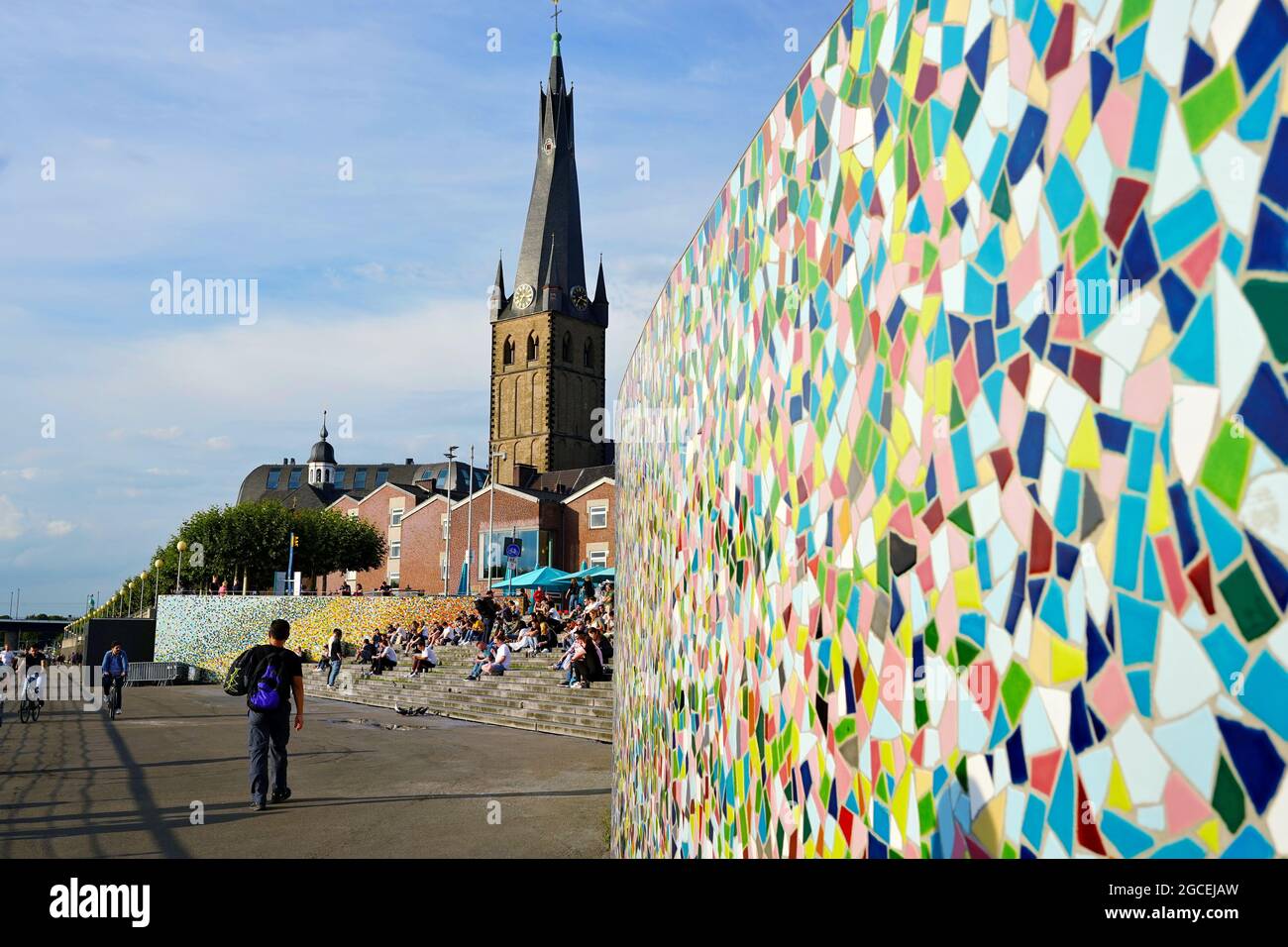 People relaxing on steps at the Rhine river promenade in Düsseldorf, Germany. Colourful 'Rivertime' mosaic wall by Hermann-Josef Kuhna. Stock Photo