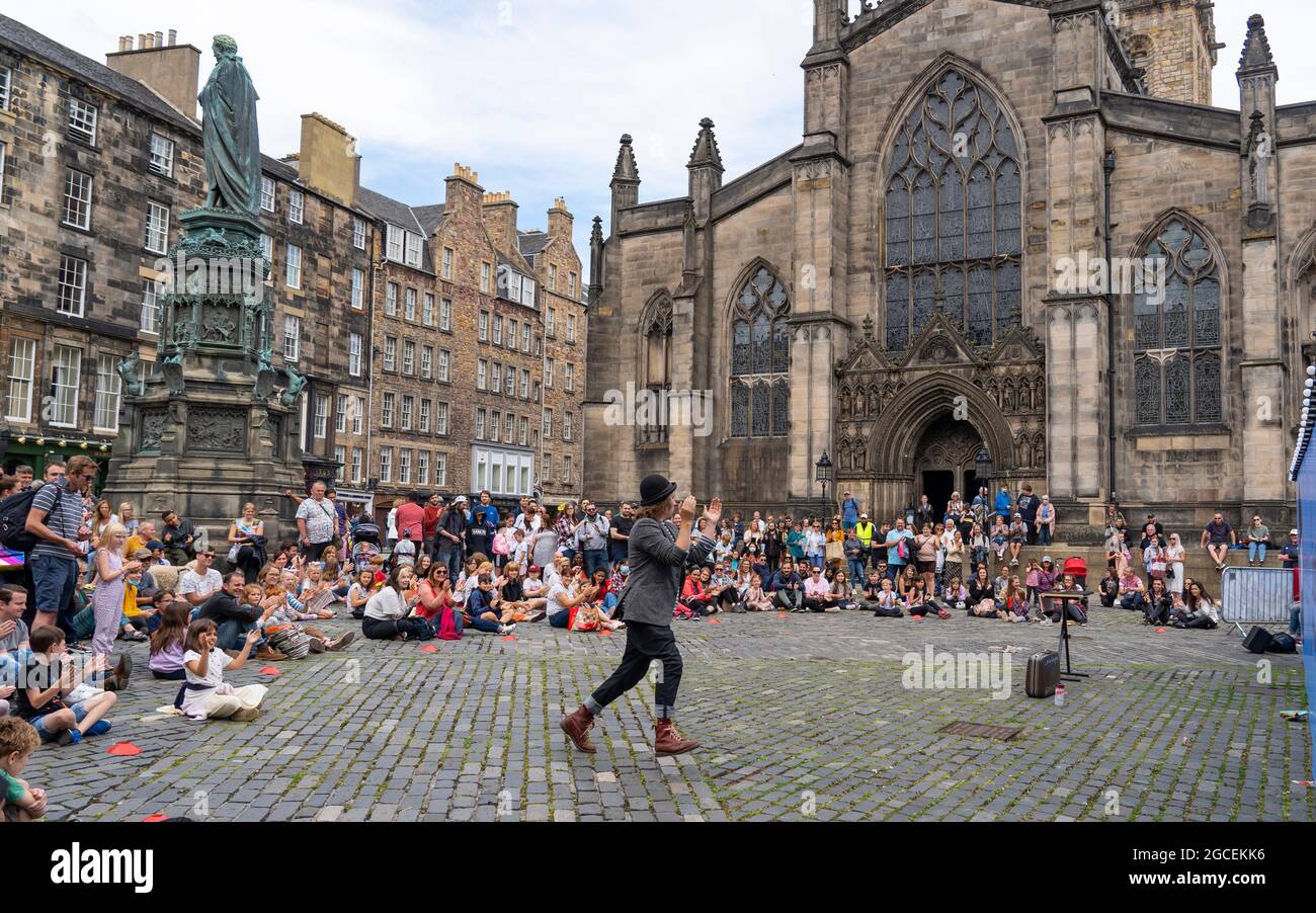 Edinburgh, Scotland, UK. 8th August  2021. On a sunny Sunday afternoon the Royal Mile was busy with visitors looking for the limited street entertainment provided during the much scaled back Edinburgh Fringe Festival this year. Two stages are provided for performers and these proved popular throughout the day. Pic; Crowd watches performer on Parliament Square in front of St Giles Cathedral. . Iain Masterton/Alamy Live news. Stock Photo