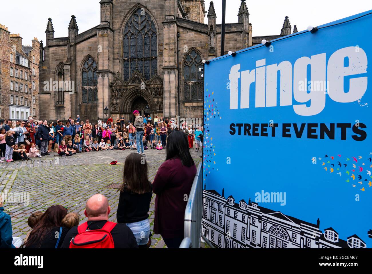 Edinburgh, Scotland, UK. 8th August  2021. On a sunny Sunday afternoon the Royal Mile was busy with visitors looking for the limited street entertainment provided during the much scaled back Edinburgh Fringe Festival this year. Two stages are provided for performers and these proved popular throughout the day. Pic; Crowd watches performer on Parliament Square in front of St Giles Cathedral. . Iain Masterton/Alamy Live news. Stock Photo
