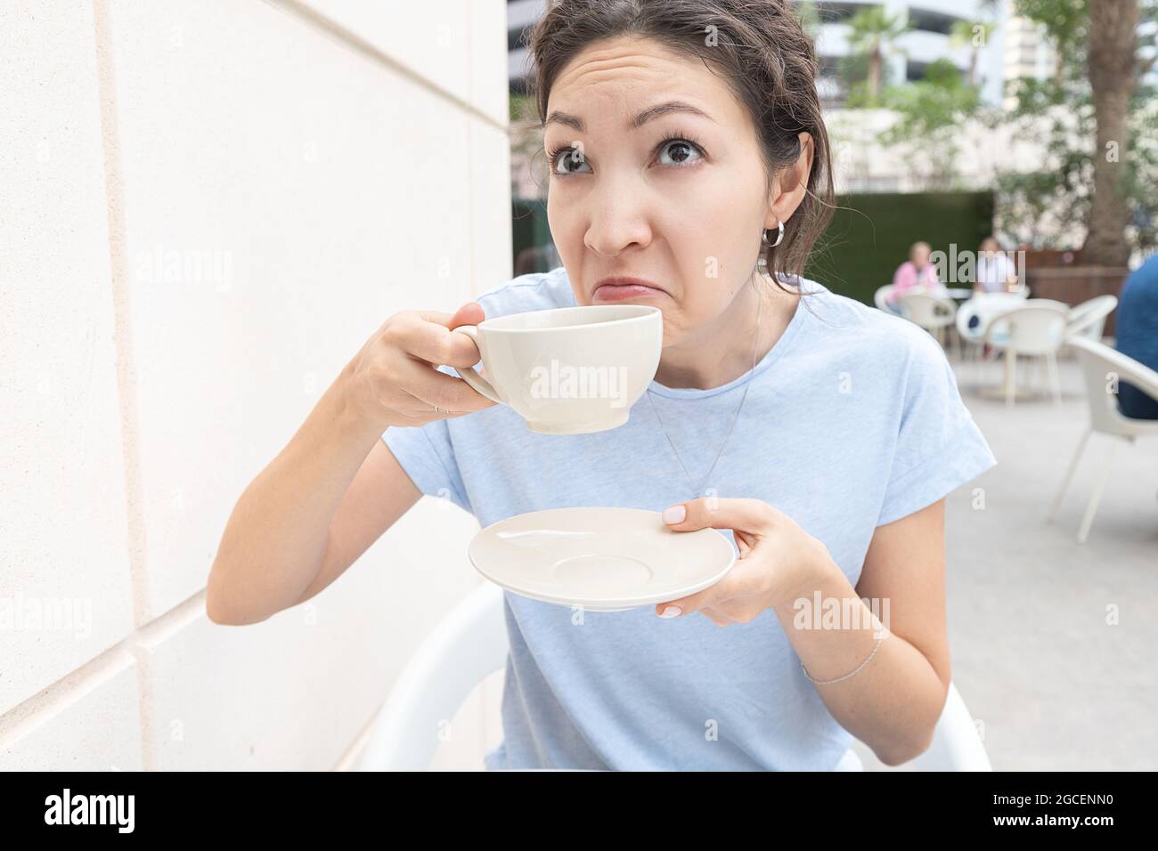 Woman takes a sip of coffee and makes a disgusting grimace. The concept of bad smell or trouble waking up and insomnia Stock Photo
