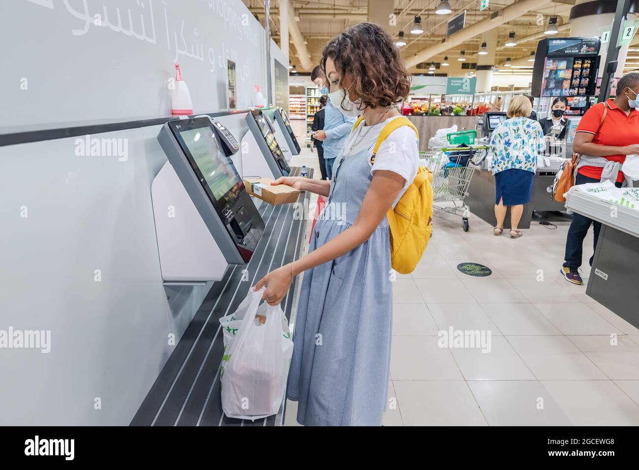 23 February 2021, Dubai, UAE: woman wearing face mask scans her supermarket purchases at a self-service checkout to make it safer to avoid contact wit Stock Photo