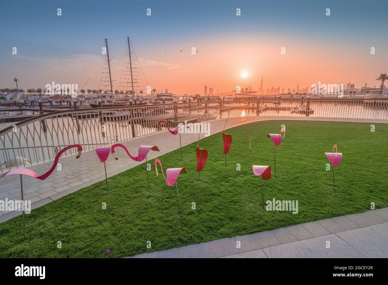 decorative figurines of pink flamingos on the boardwalk and white arch against the background of the bay with ships and yachts in the marina Creek Har Stock Photo