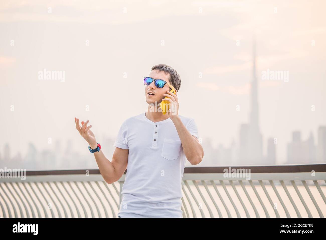 Chatty man is on the phone for work or for fun and gestures against the backdrop of Dubai Creek and the Burj Khalifa Stock Photo