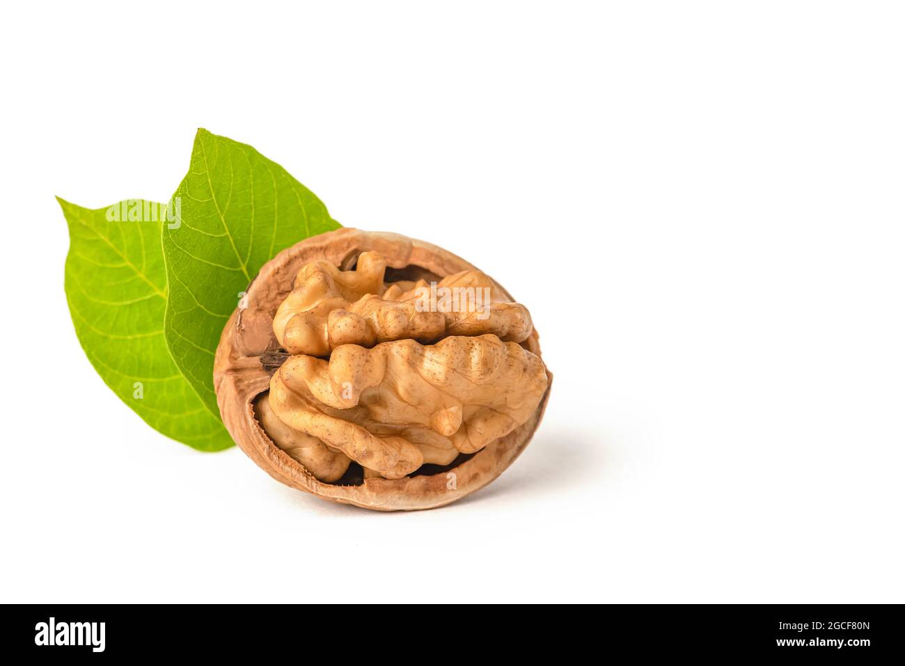 Walnut fruits lie on a white isolated background. Peeled walnut and green leaves with shadow. White isolate for design and project insertion Stock Photo