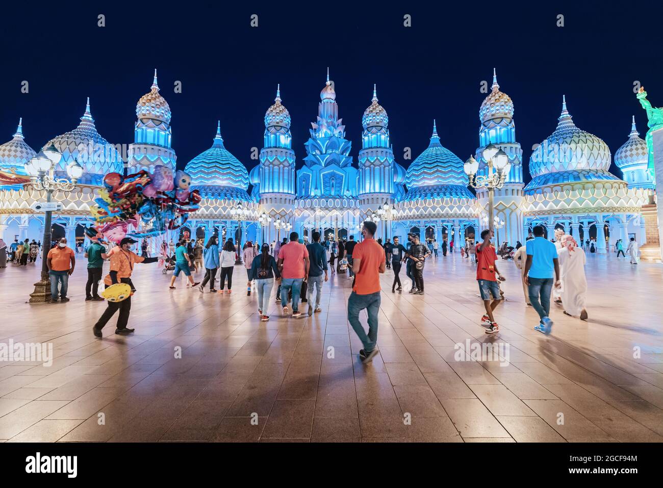 26 February 2021, UAE, Dubai: Visitors and tourists walk through the streets of the Global Village illuminated in the evening with pavilions of many c Stock Photo