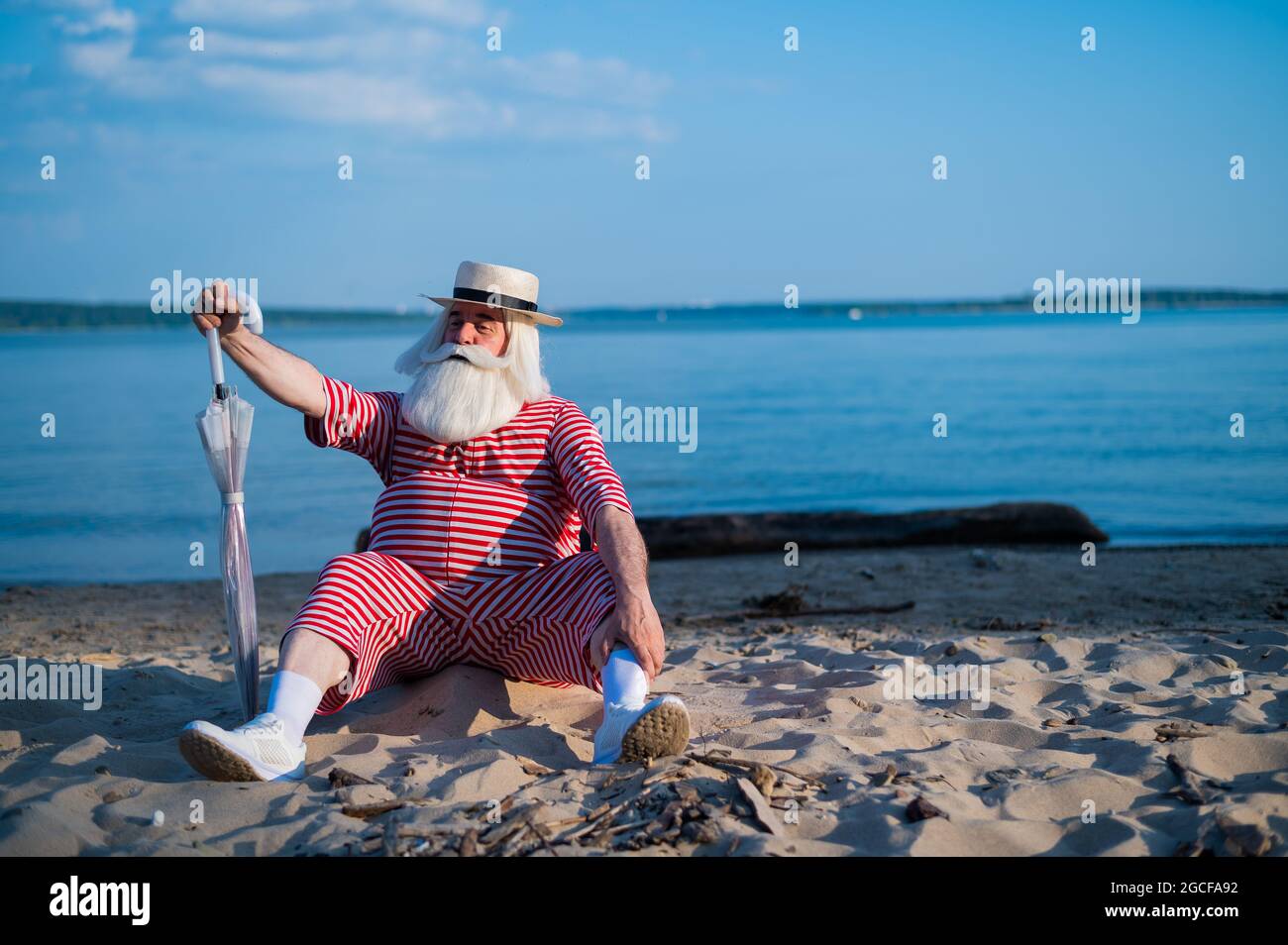 An old man in a classic bathing suit walks along the beach with an