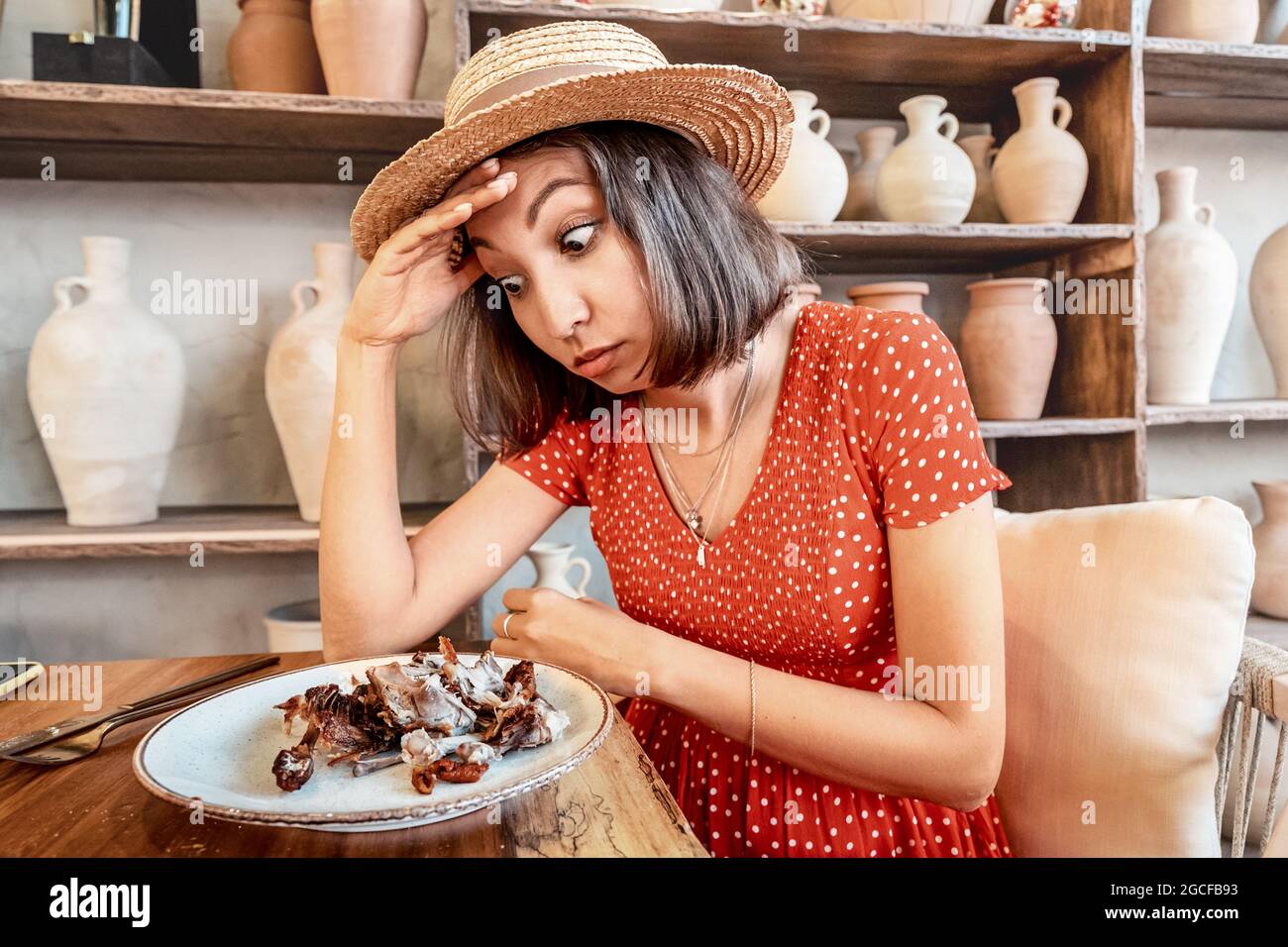 Woman with a strong appetite finishes the meal in restaurant. Bones of a fried chicken in a plate. The concept of overeating and gluttony and deliciou Stock Photo