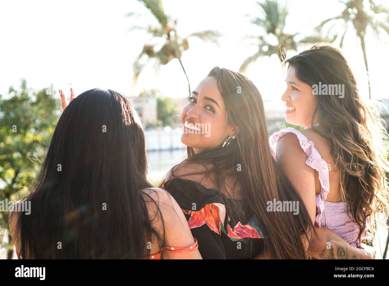 Three young friends outdoors enjoying a nice summer afternoon. Latin girls  sitting together with their backs turned and one of them looking at the cam  Stock Photo - Alamy
