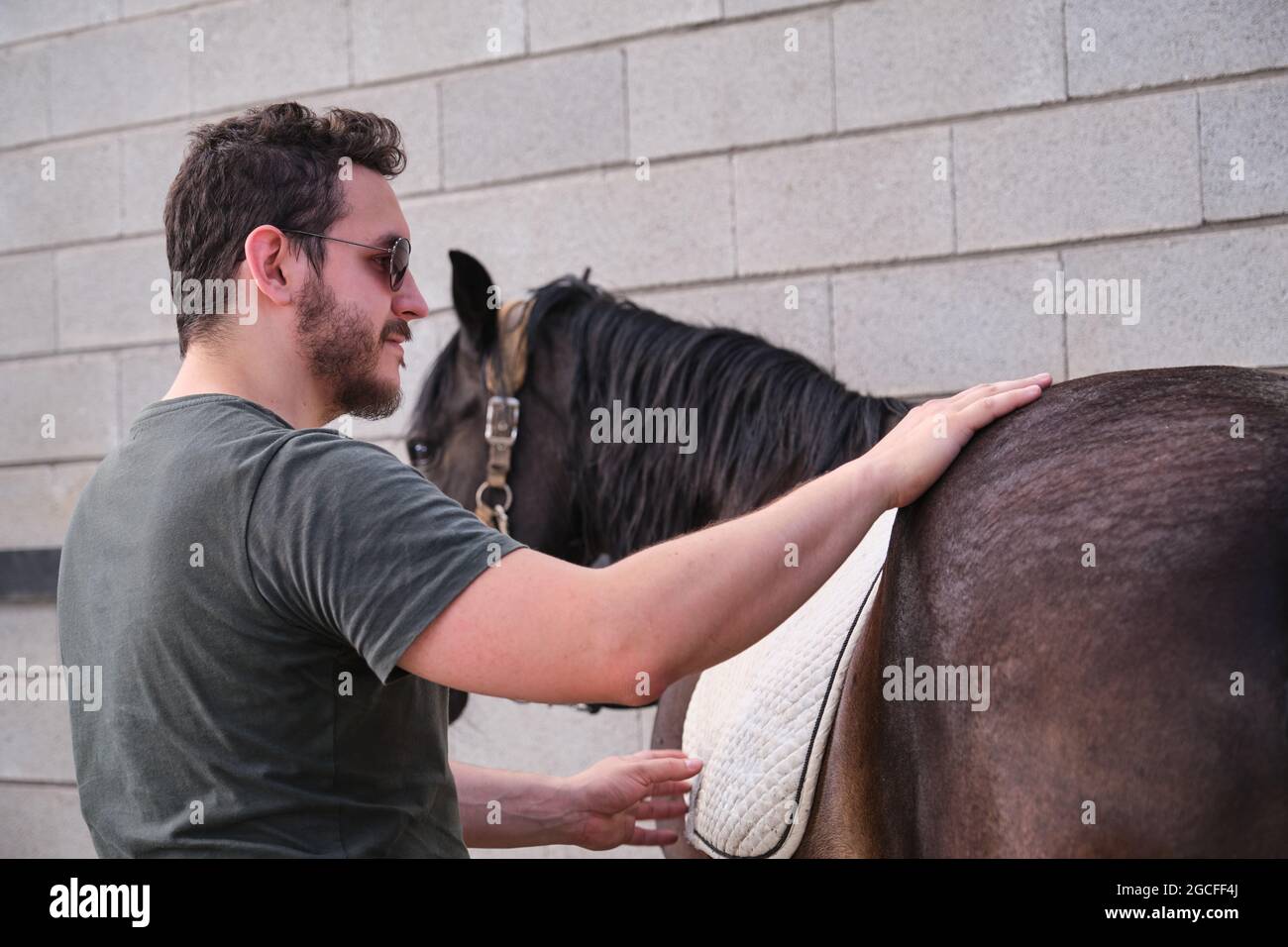 Young latin man putting on the saddle blanket to his horse and stroking