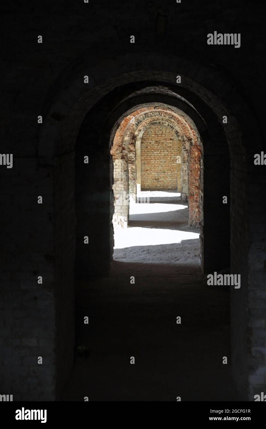 A through corridor through the casemates of the defensive barracks in the rays of sunlight. Arch. Stock Photo