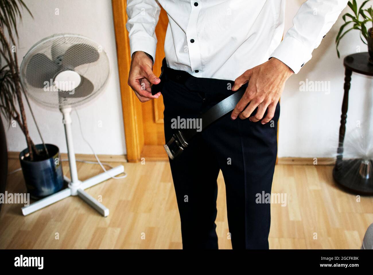 Man wears belt. Young businessman in casual suit with accessories. Fashion and clothing concept. Groom getting ready in morning before ceremony. Stock Photo
