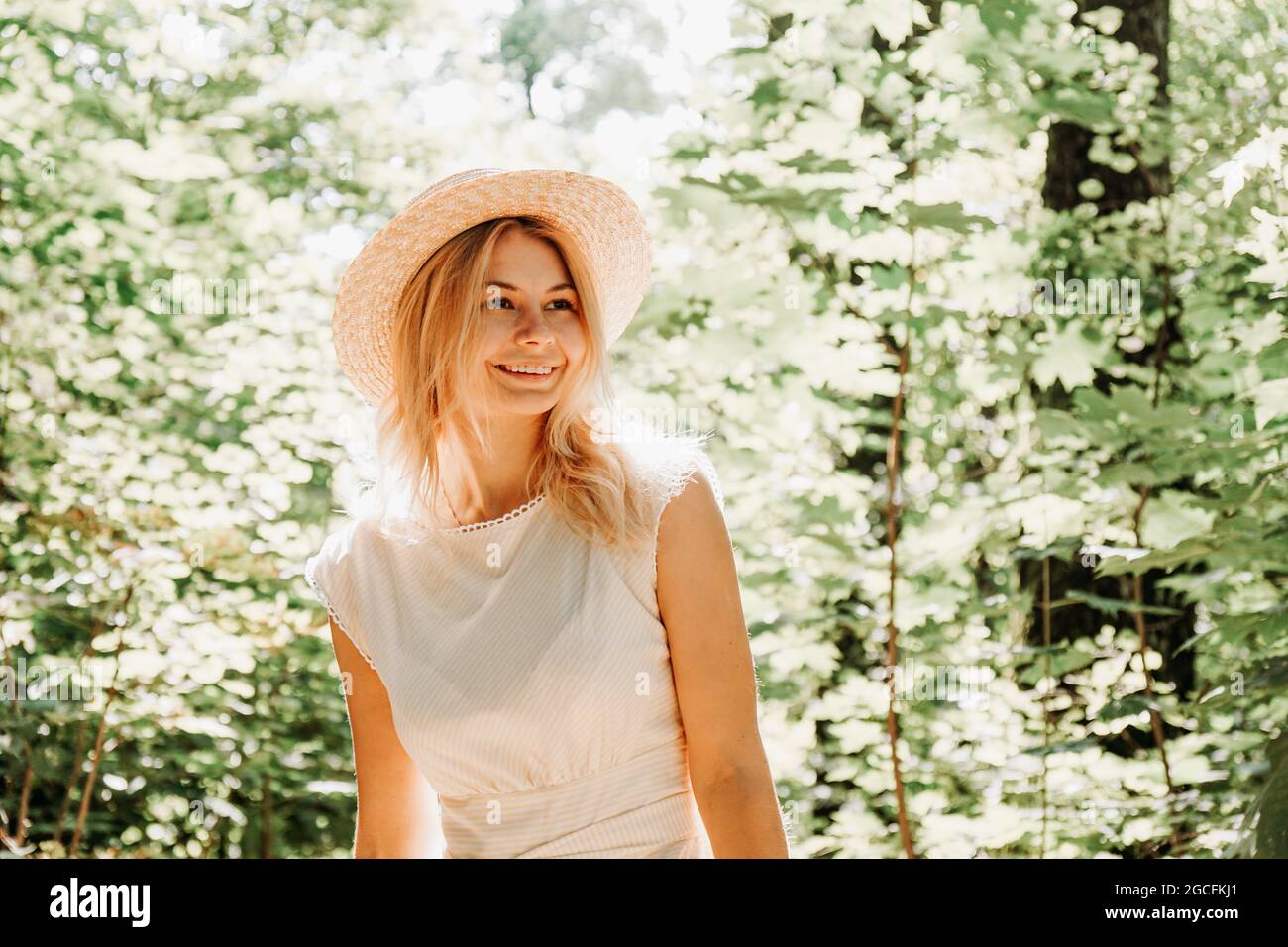 Beautiful young woman in a straw hat and white dress in a green park or ...