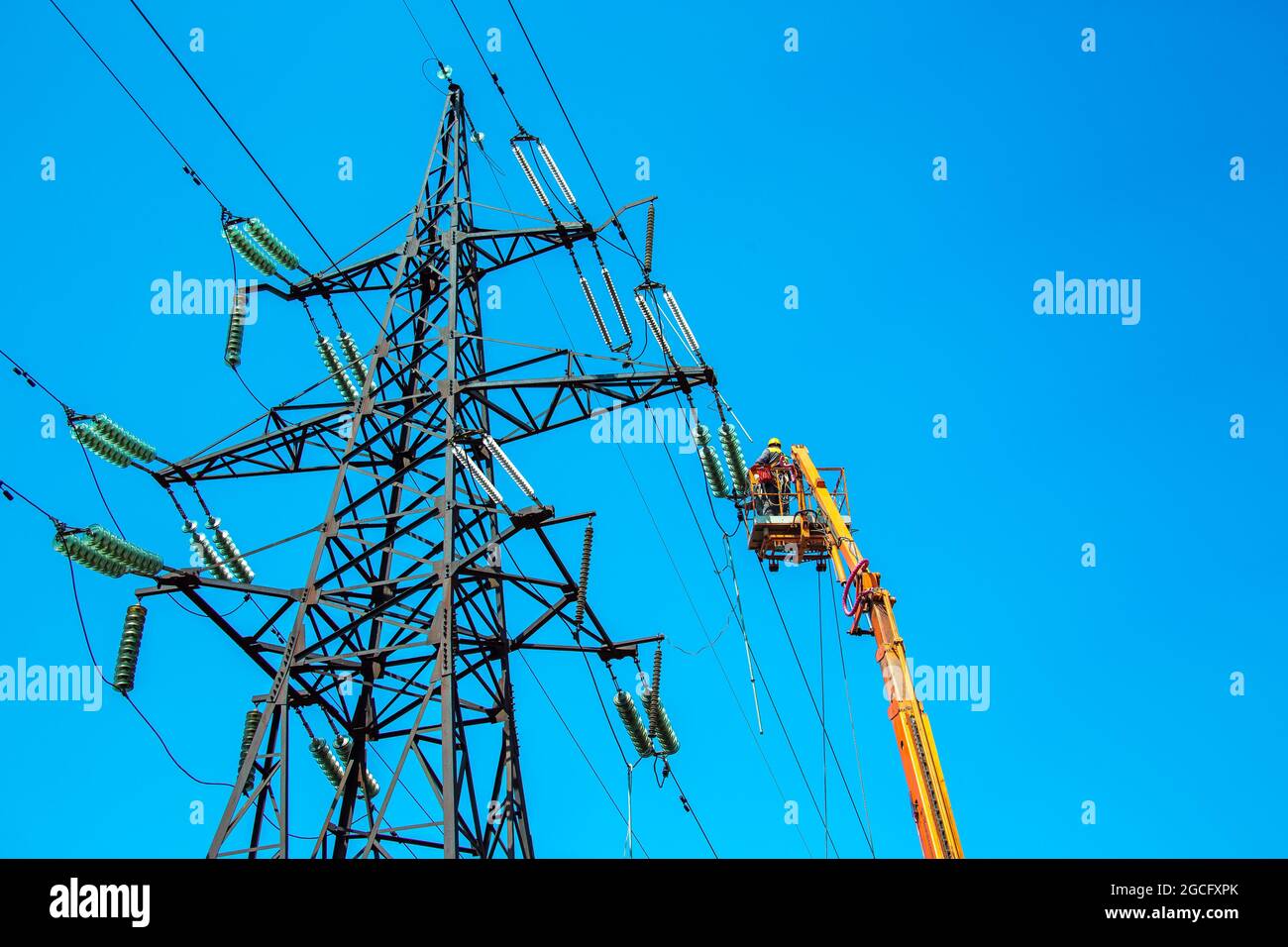 High voltage power line transmission tower workers with crane and blue