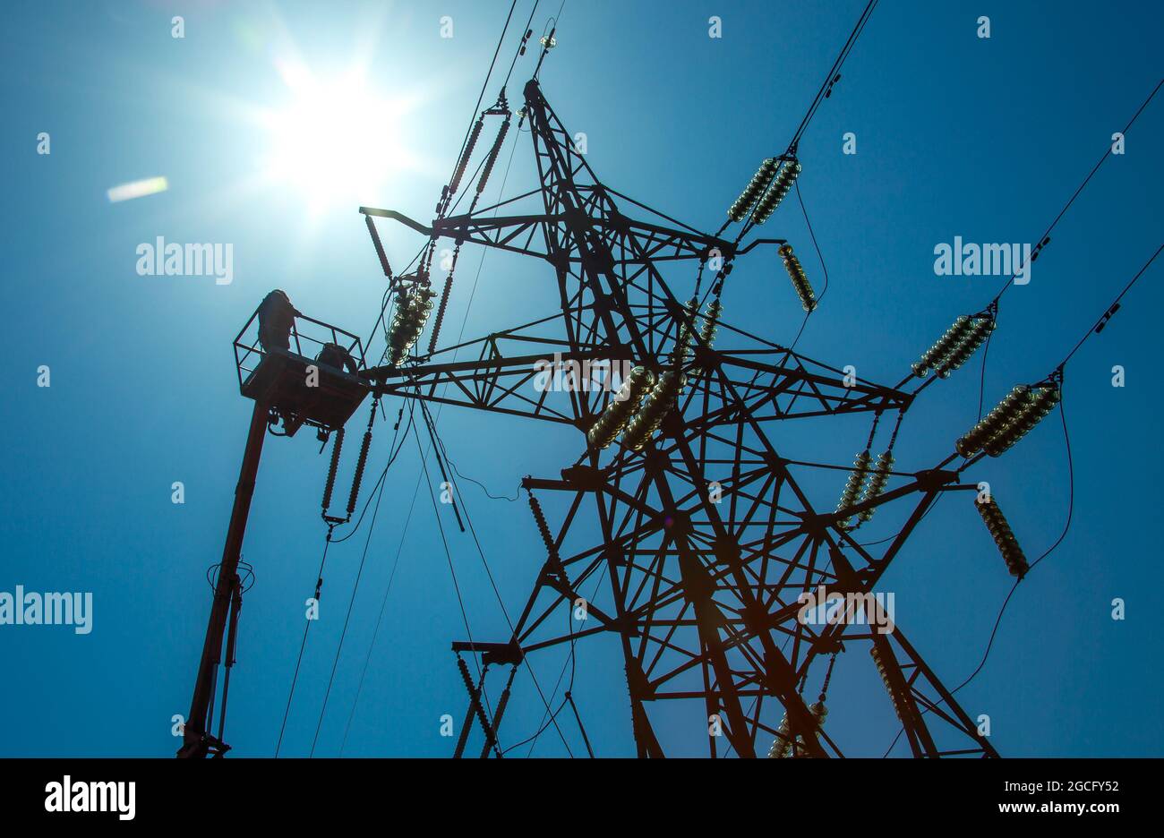 High voltage power line transmission tower workers with crane and blue
