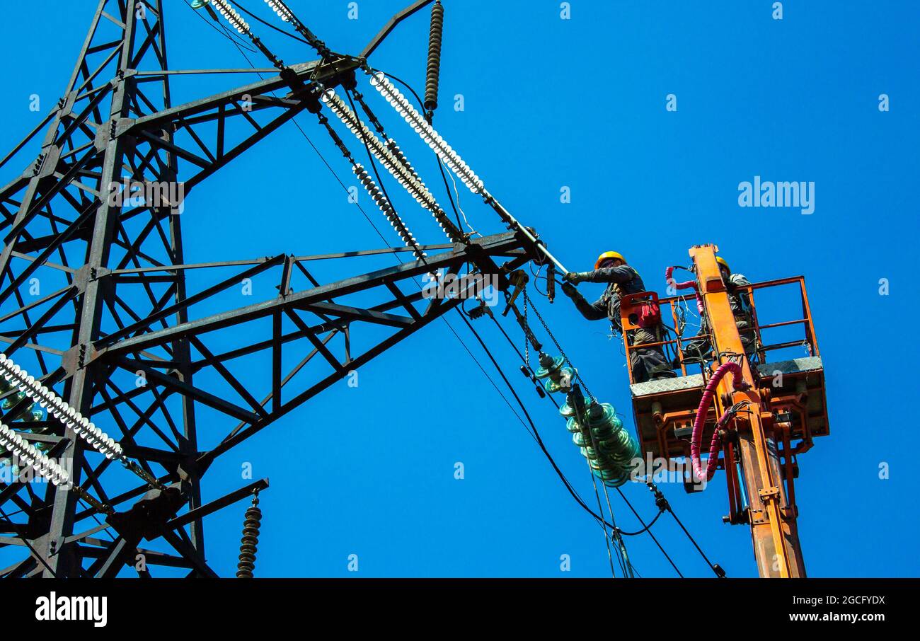 High voltage power line transmission tower workers with crane and blue