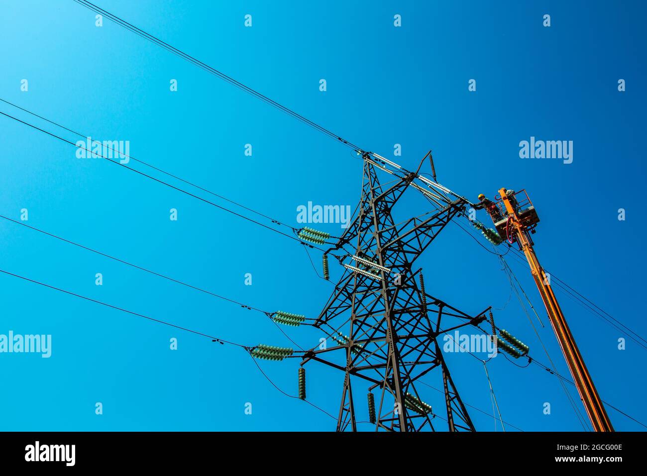 High voltage power line transmission tower workers with crane and blue