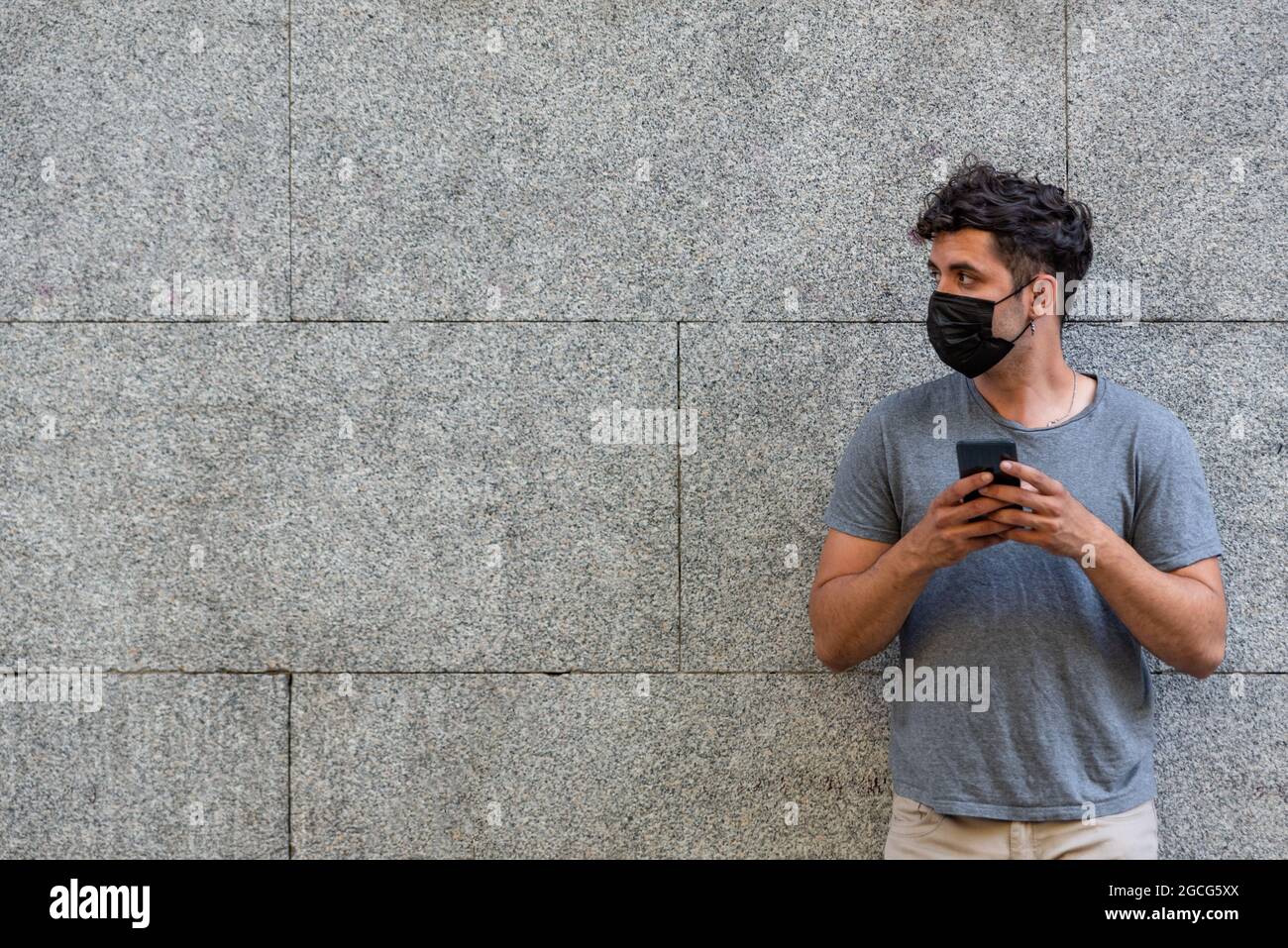 Young latin man with face mask using phone Stock Photo