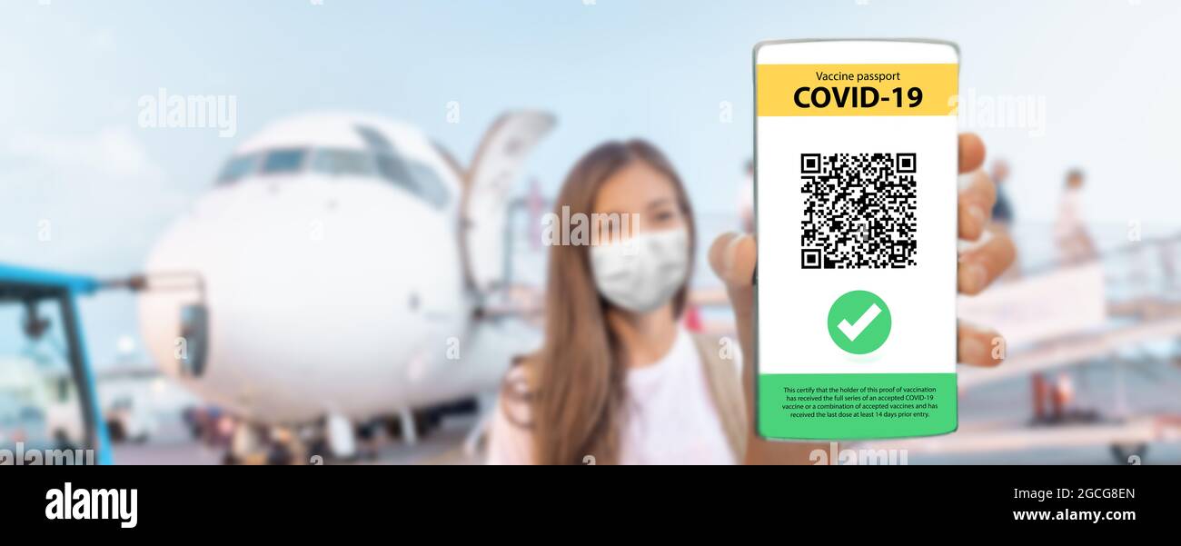 Travel vaccine passport tourist woman wearing mask arriving by plane showing immunization proof on mobile phone after flight at airport. Girl walking Stock Photo