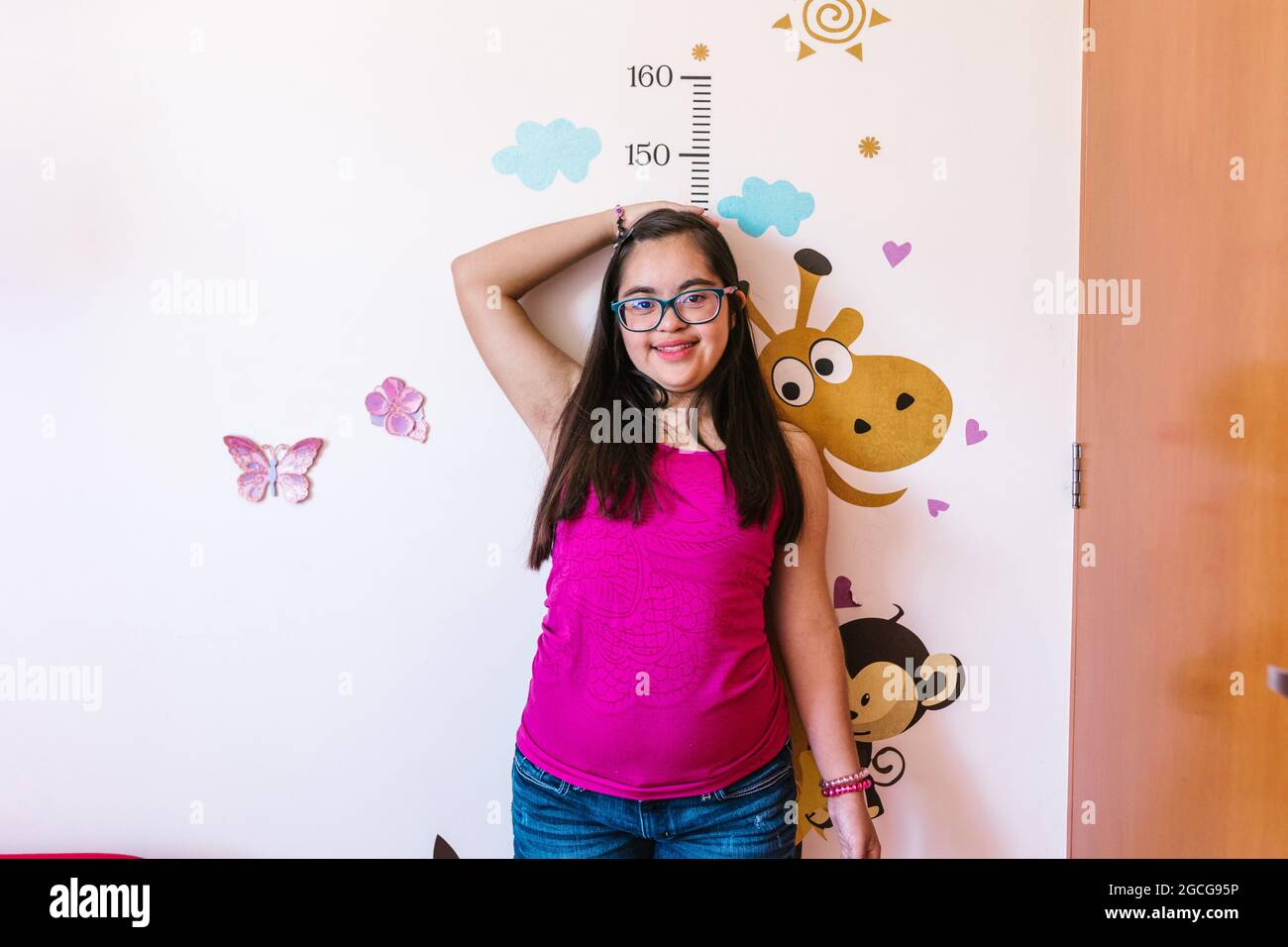 Hispanic teen girl with down syndrome measuring her height on the wall, in disability concept in Latin America Stock Photo