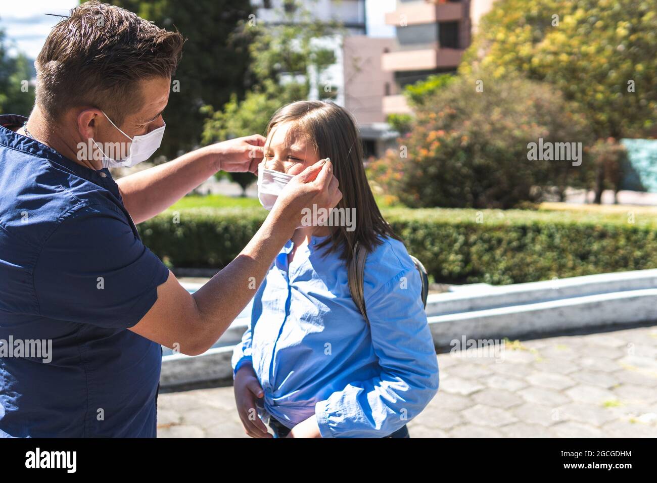 Father putting the mask on his daughter at the entrance to classes. Back to school Stock Photo