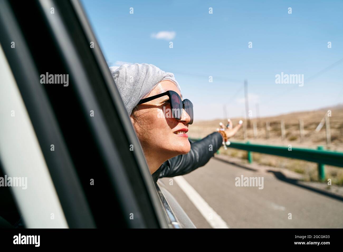 asian woman tourist sticking head out of rear window of a car and enjoying a road trip Stock Photo