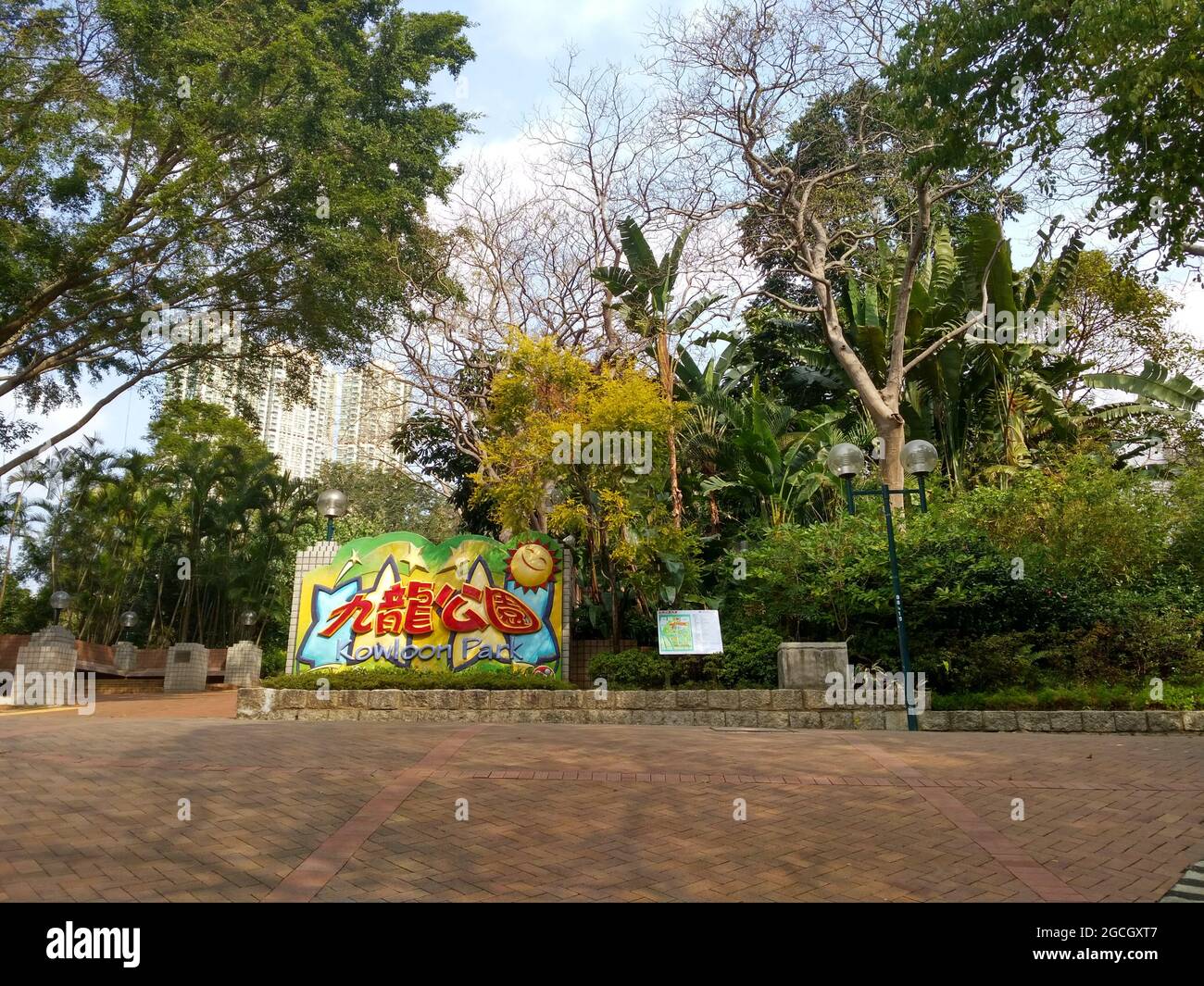 The entrance to Kowloon Park in Hong Kong with brick paths leading to a large colorful sign in Chinese with a happy sun and stars plus a park map Stock Photo