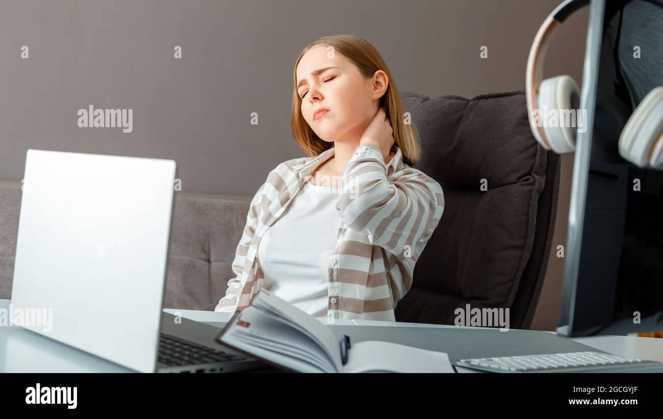Young woman suffers from neck pain. Tired woman have headache and cervical back pain while sitting working in office or at home workspace. Long web Stock Photo