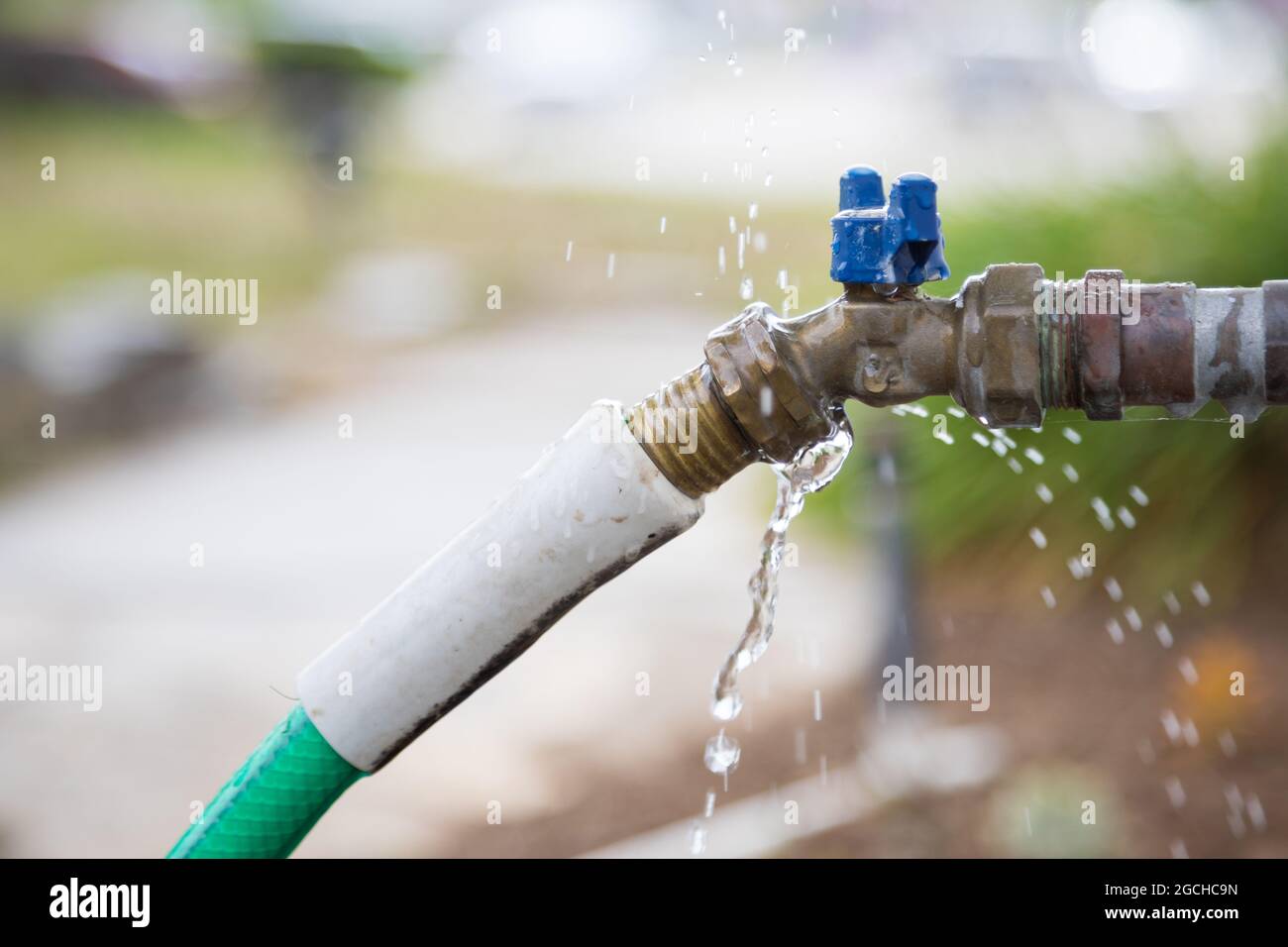 Exterior water faucet with garden hose leaking water Stock Photo