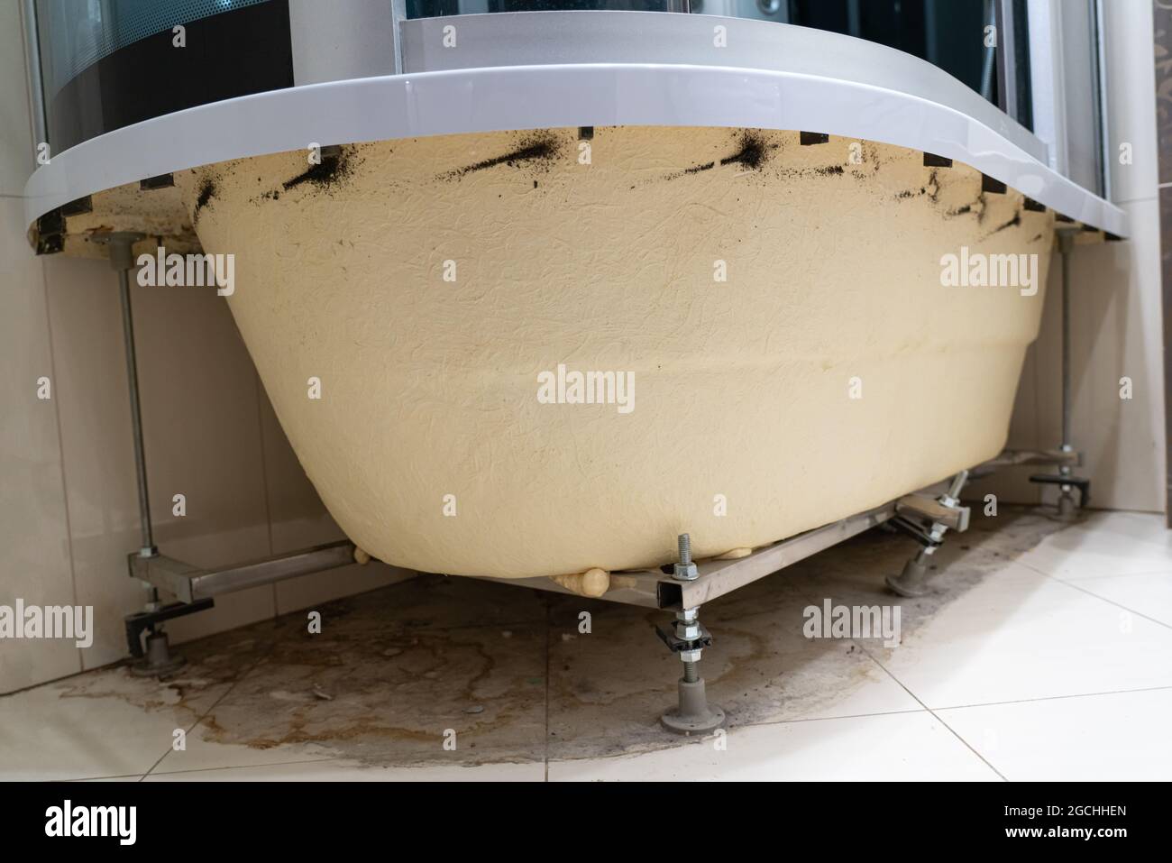 dirty puddle, dirt, hair, dust, mold, bacteria, fungus on the floor under the bathroom. inner side of acrylic bathtub without decorative panel. rusty Stock Photo