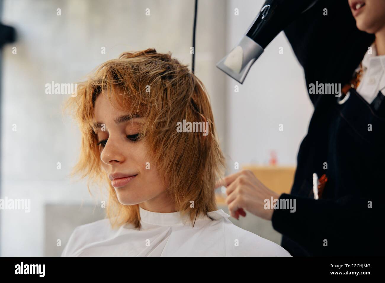 Young male Asian hairdresser wearing apron drying handsome young man's hair in a modern barber shop while concentrating on work Stock Photo