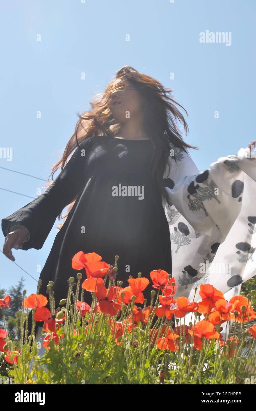 Low angle view of a south asian young girl posing behind red poppy flowers in outdoor Stock Photo