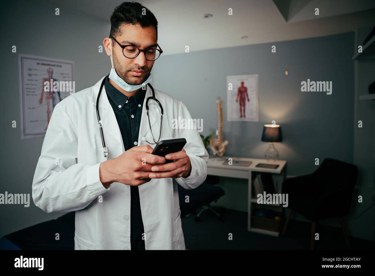 Mixed race male nurse standing in doctors office texting on cellular device Stock Photo