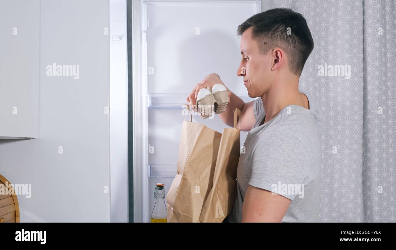 Young man puts different food products into large fridge Stock Photo