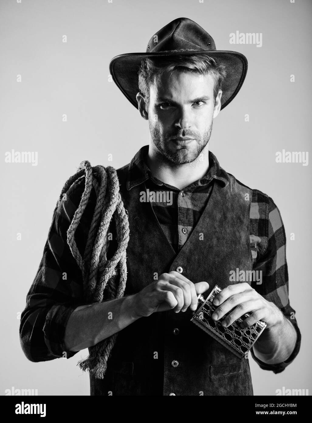 Western life. Sheriff concept. Bourbon whiskey. Western culture. Man wearing hat hold rope and flask. Lasso tool American cowboy. Brutal cowboy Stock Photo