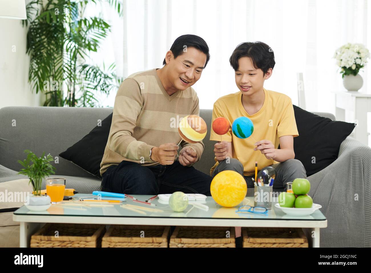 Cheerful dad and his teenage son using styrofoam balls when making solar system for school Stock Photo