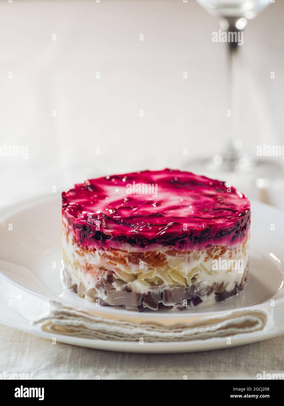 Layered salad herring under fur coat on table. Portion of traditional russian salad with herring, beet and other vegetables on white linen tablecloth. Copy space. Vertical. Stock Photo