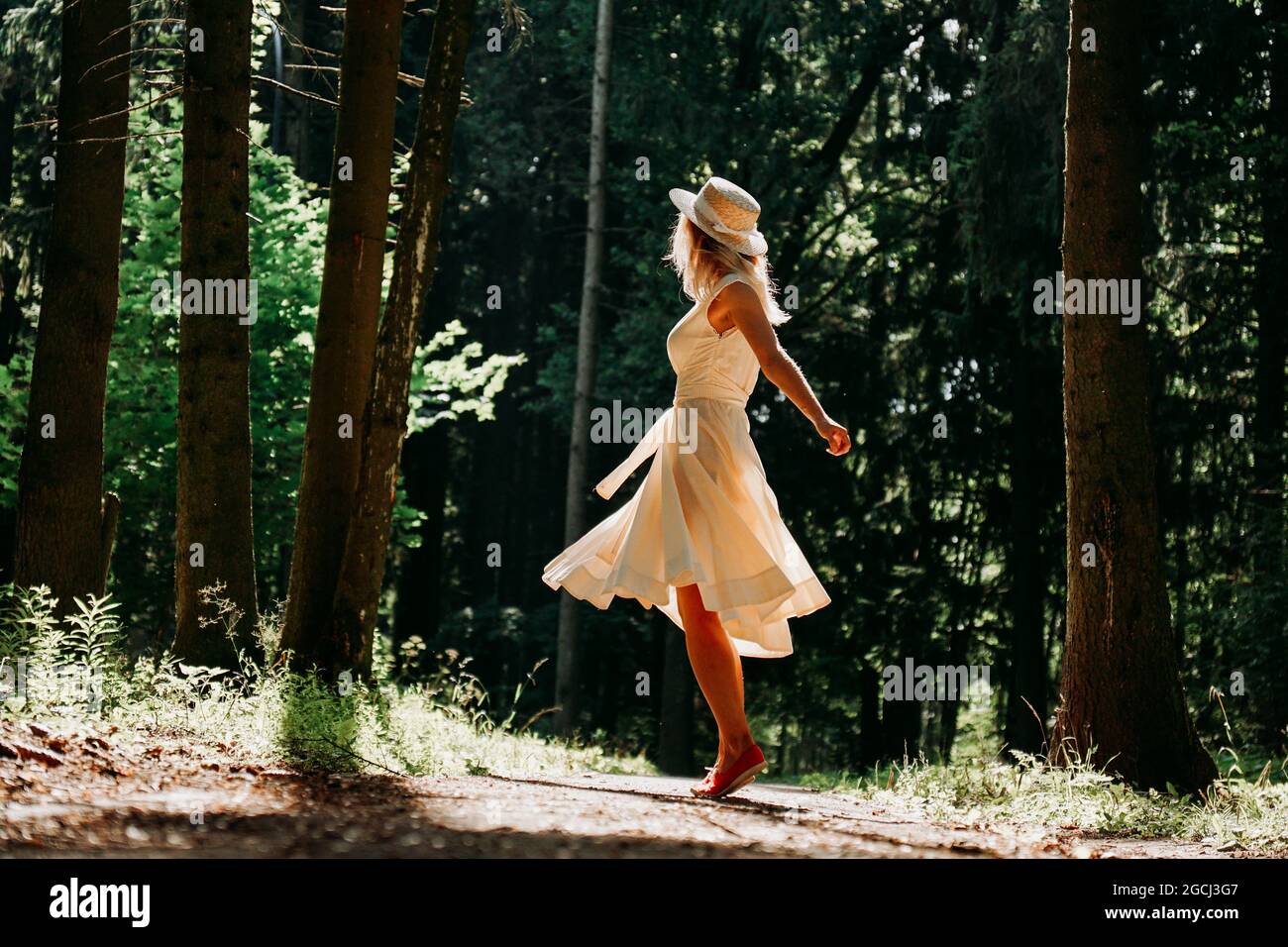 A young woman in a white dress and a straw hat walks through the woods ...