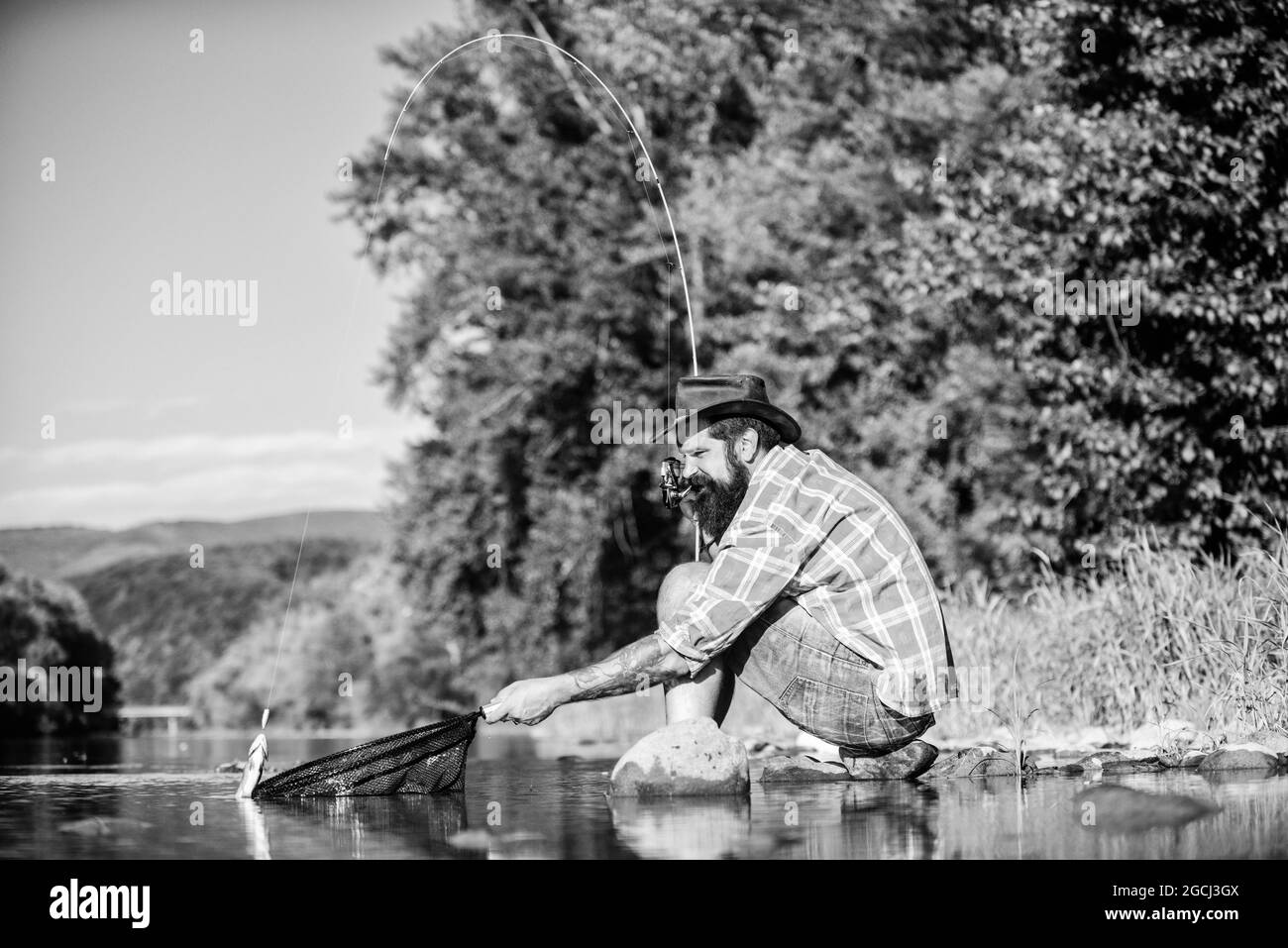 hipster fishing with spoon-bait. mature bearded man with fish on rod. successful fisherman in lake water. fly fish hobby. Summer activity. big game Stock Photo