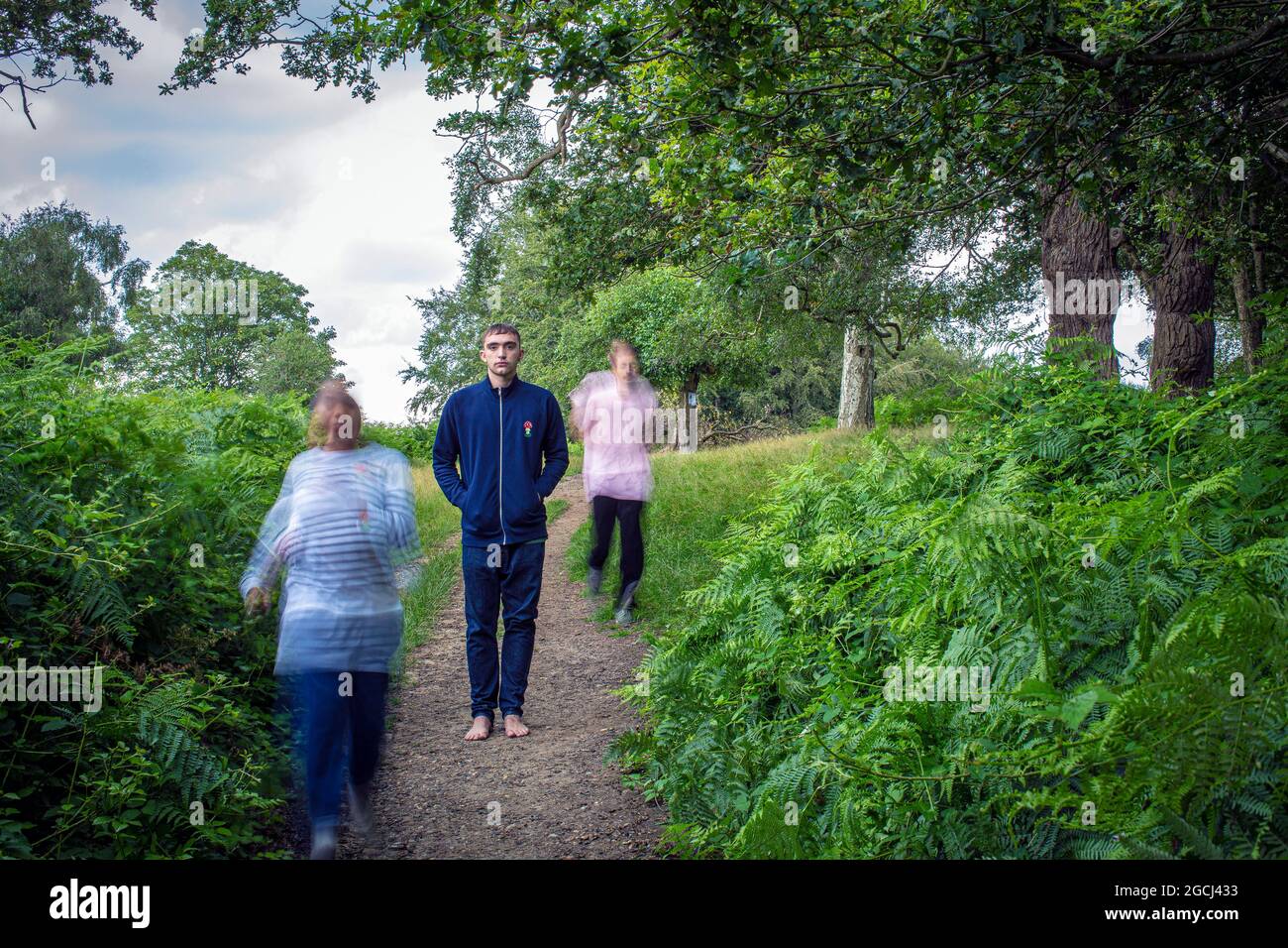 Young man standing still  in park and motion blur of two people running Stock Photo