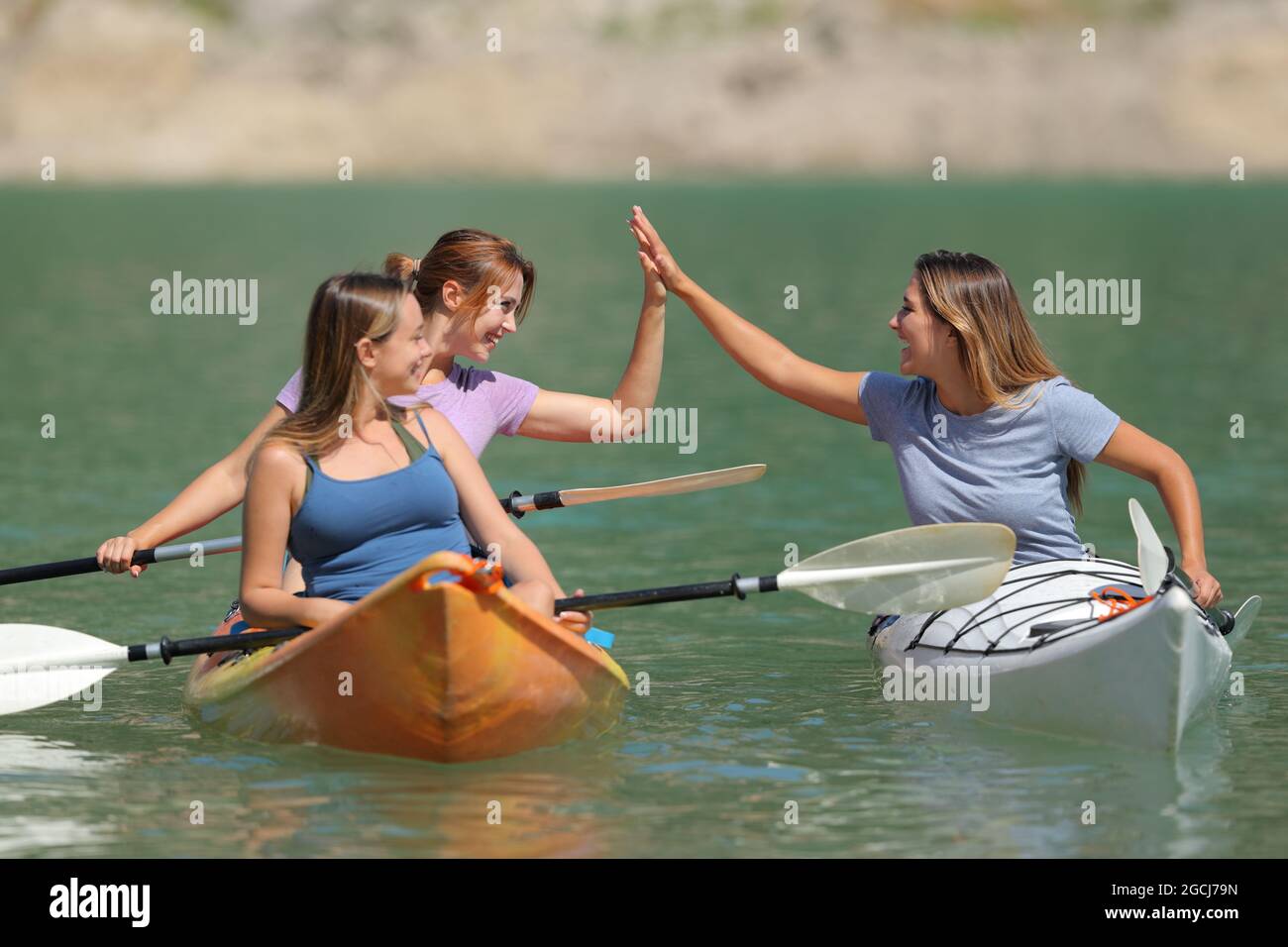 Three friends giving five enjoying a kayak day in a beautiful lake on summer vacation Stock Photo