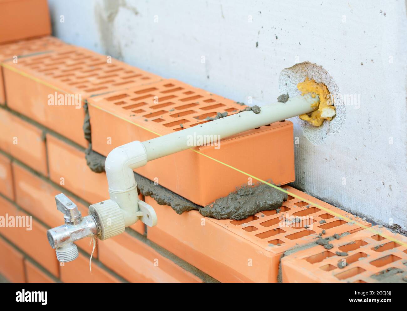 A close-up on laying face clay bricks to a concrete block wall with an outside water spigot, garden faucet. Stock Photo
