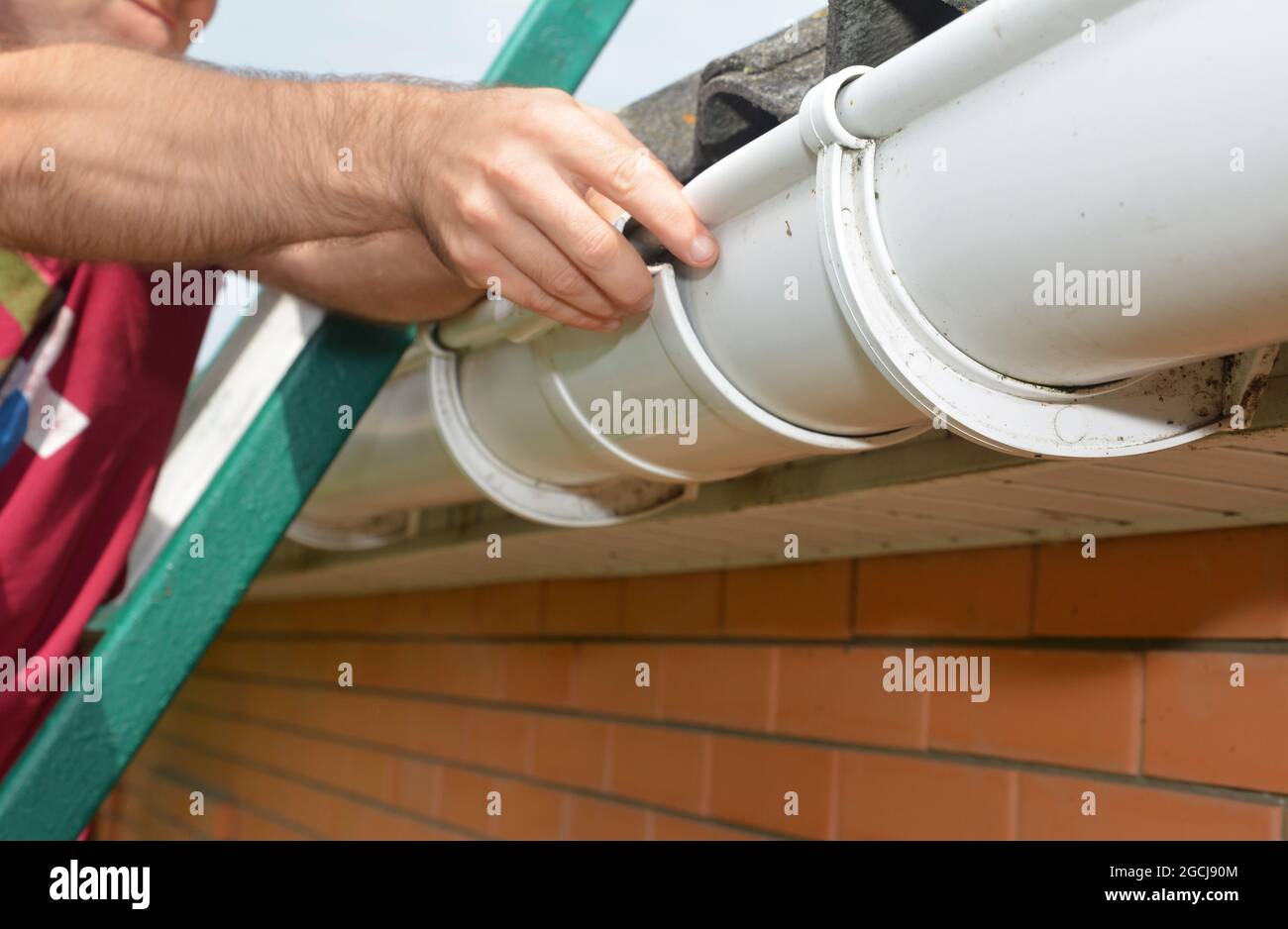 Roof gutter installation. A man on a ladder is installing a roof gutter